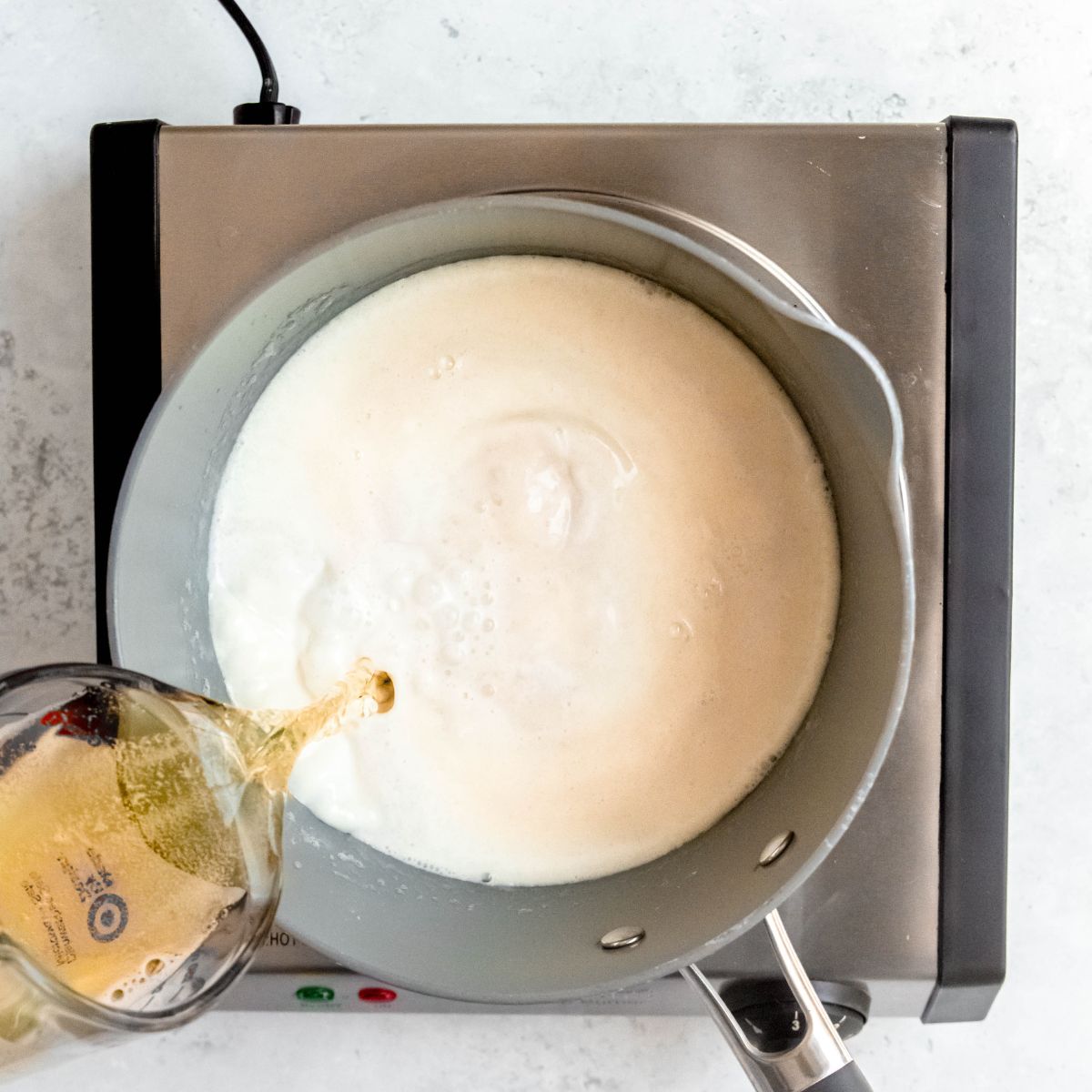 Beer being poured into a pot of warm milk on a portable burner.