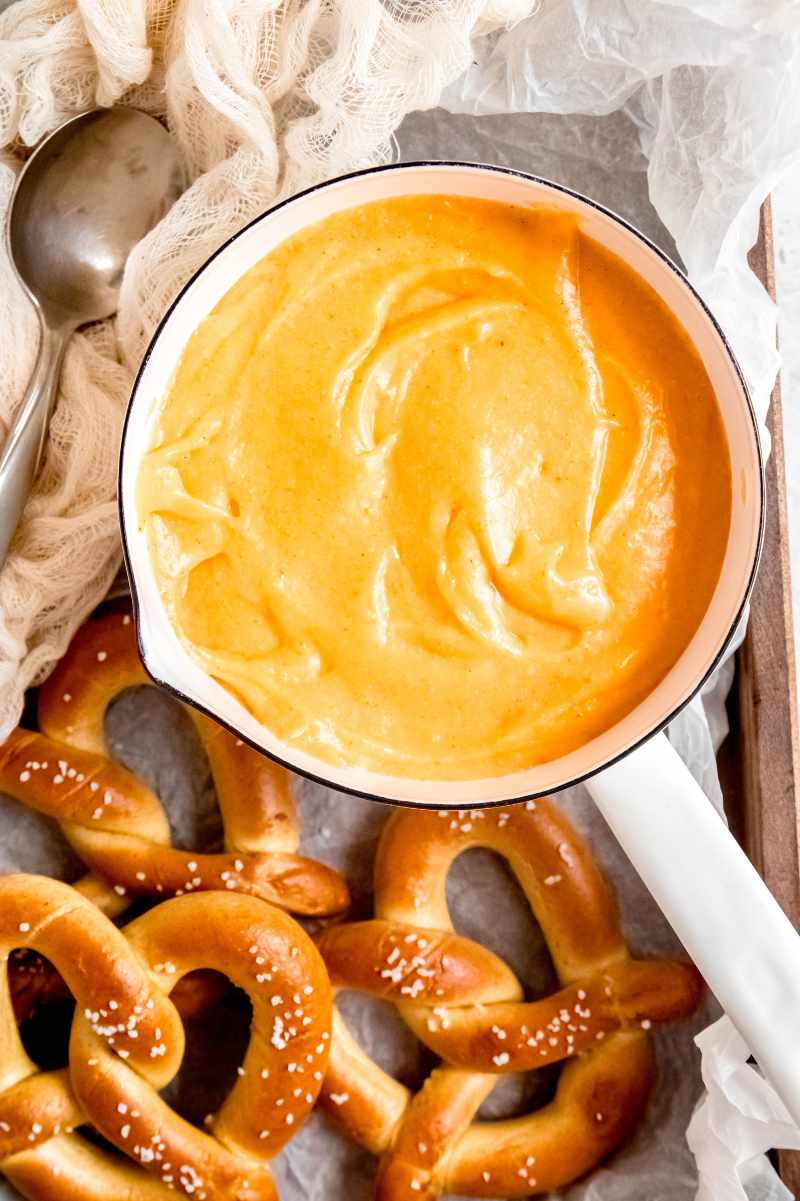 Overhead of a white saucepan filled with a warm cheese dip appetizer with soft pretzels around it.