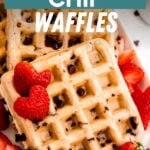 Homemade waffles studded with chocolate morsels on a white platter surrounded by cut strawberries. A text overlay reads, "Chocolate Chip Waffles."