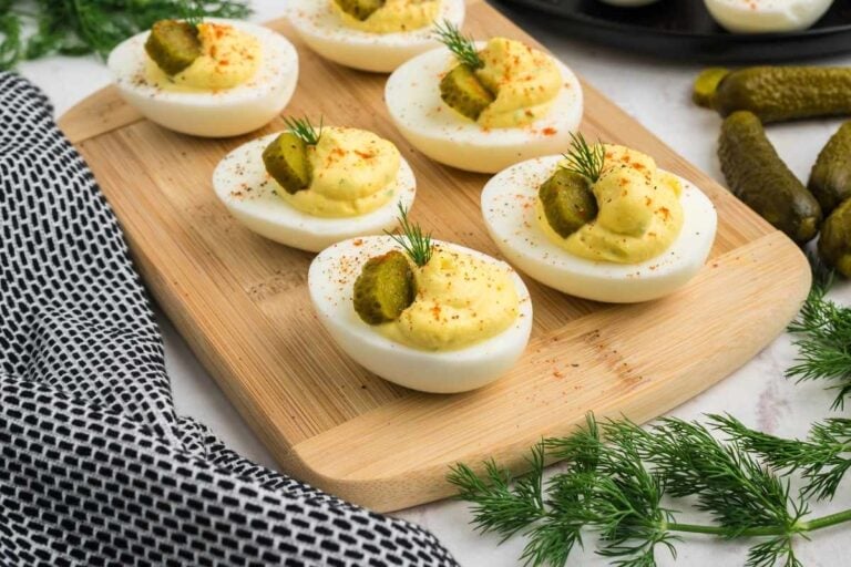 Flavorful deviled eggs on a serving board with fresh herbs and cornichons nearby.