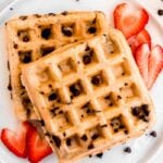 Two homemade waffles on a white plate with cut strawberries.