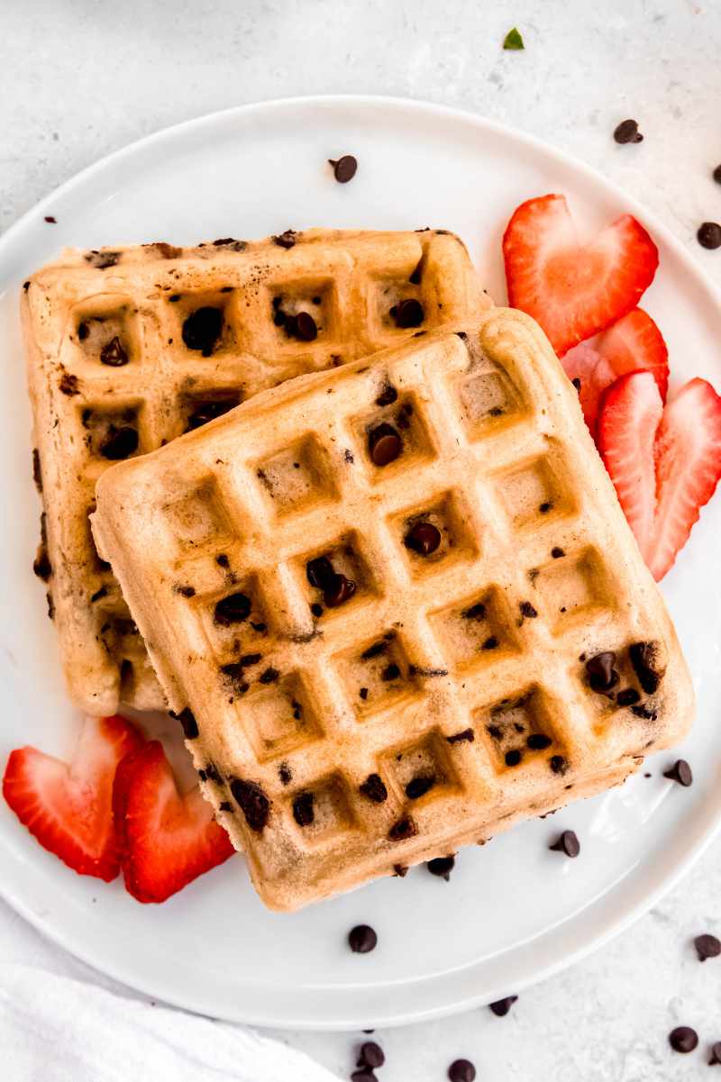 Two homemade waffles on a white plate with cut strawberries.