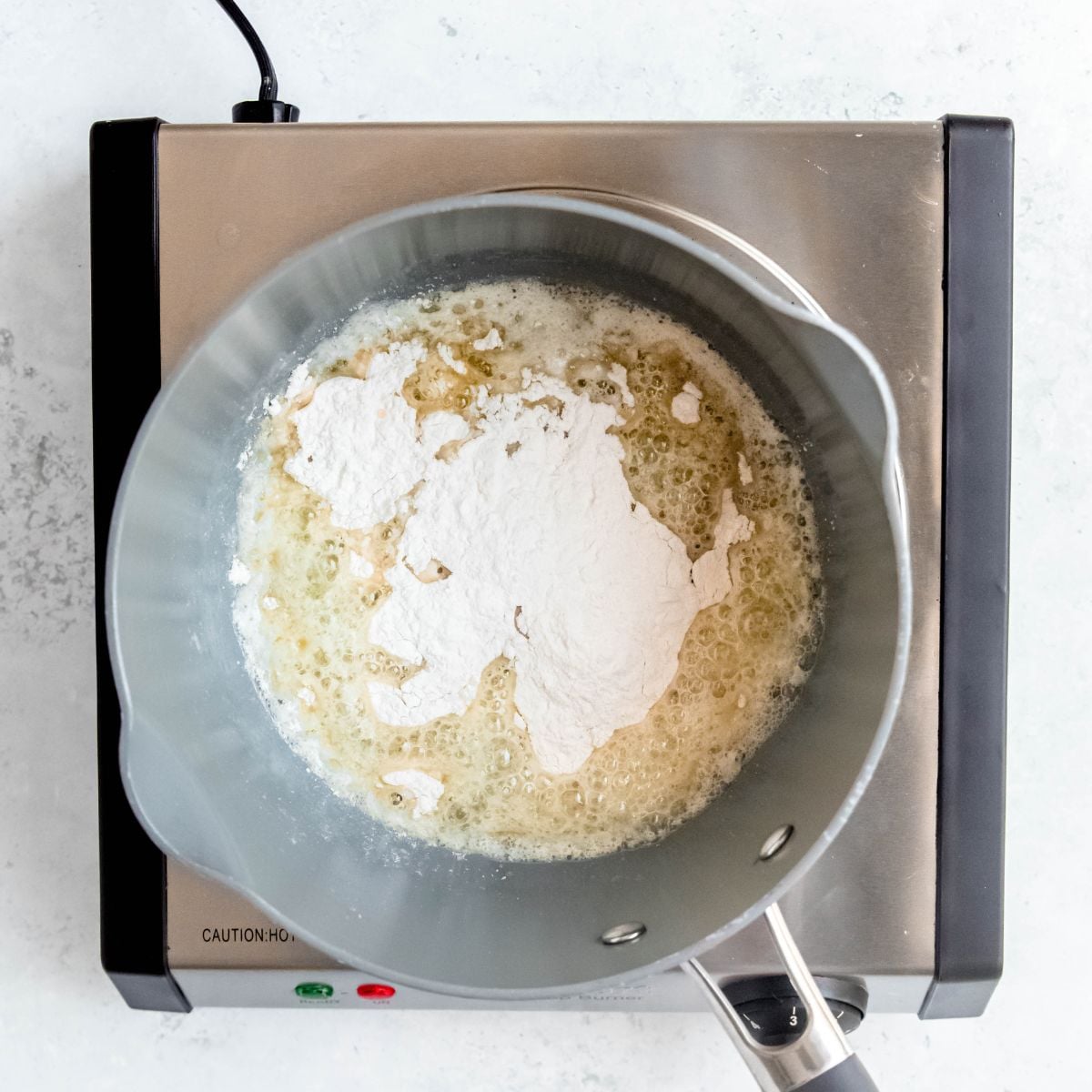 Melted butter and flour combining into a roux in a pot on a portable burner.