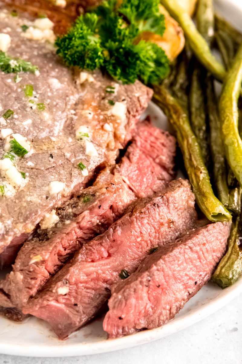 Tight view of a sliced steak topped with garlic butter on a plate.