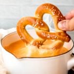 A soft pretzel dipped into a pot of beer cheese, with the cheese stretching as it's lifted.
