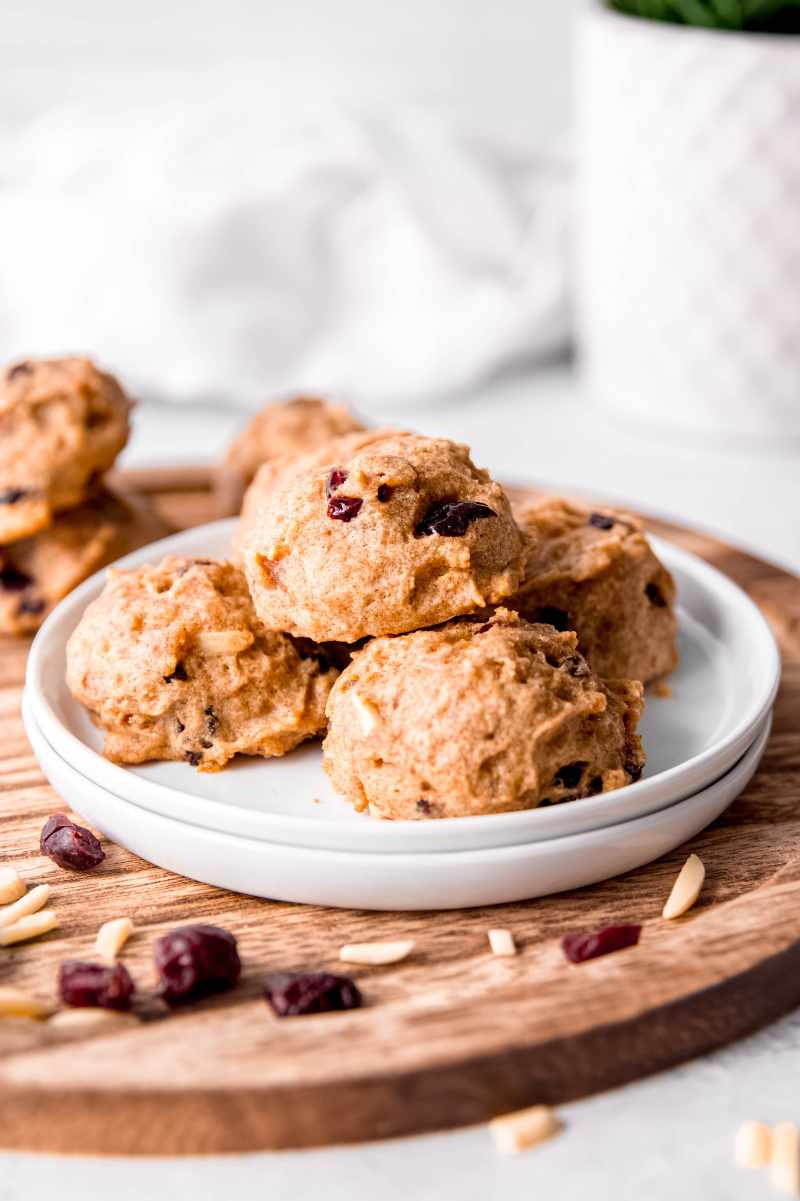 Soft cranberry almond cookies stacked on a white plate with additional cranberries and almonds around them.