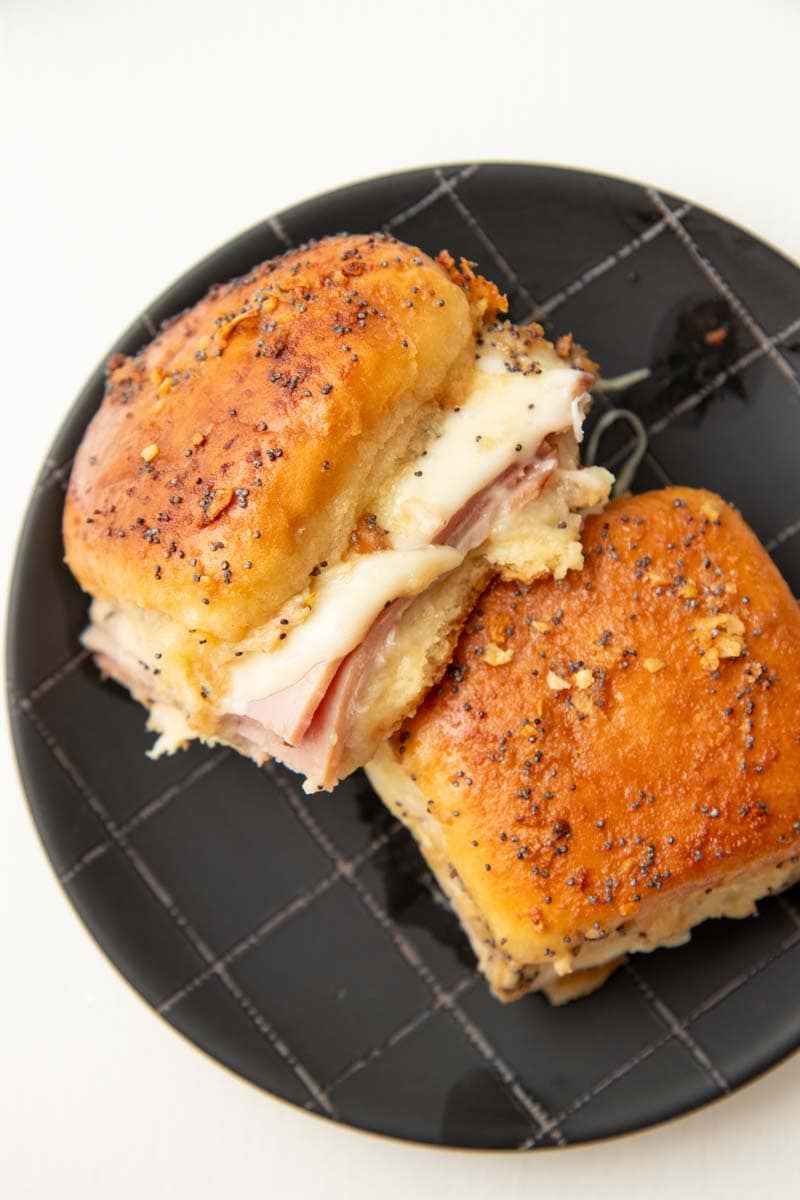 Close view of two ham and swiss sliders on a dark plate.