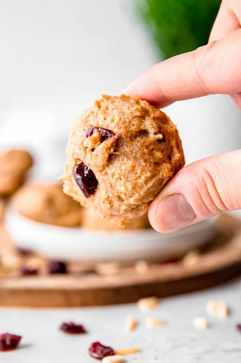 Two fingers hold up a soft cranberry cookie on a light background.
