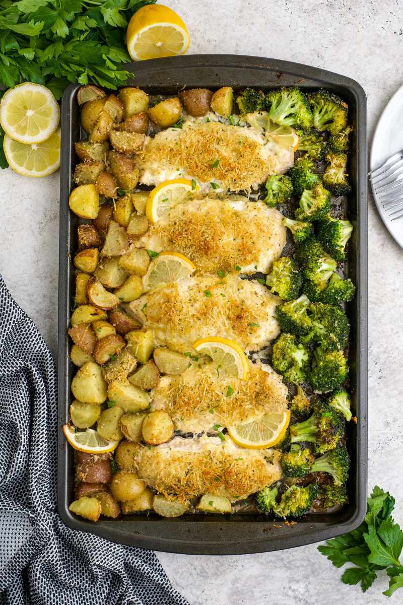 Overhead of a full sheet pan of chicken and vegetables topped with parmesan and citrus slices.