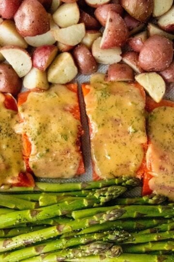 Sheet pan covered with a silicon baking sheet, salmon, asparagus, and potatoes, ready to be cooked.