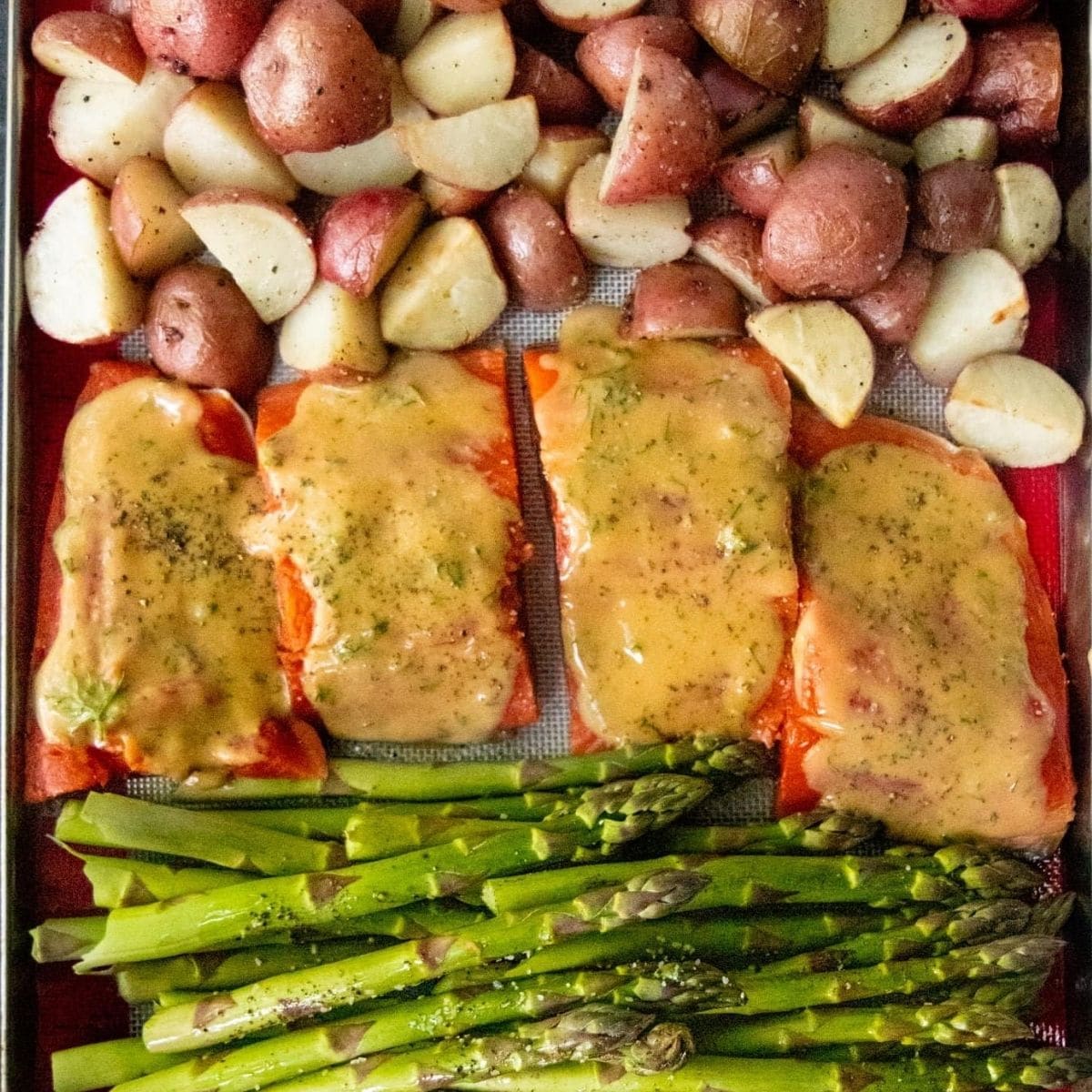 Sheet pan covered with a silicon baking sheet, salmon, asparagus, and potatoes, ready to be cooked.