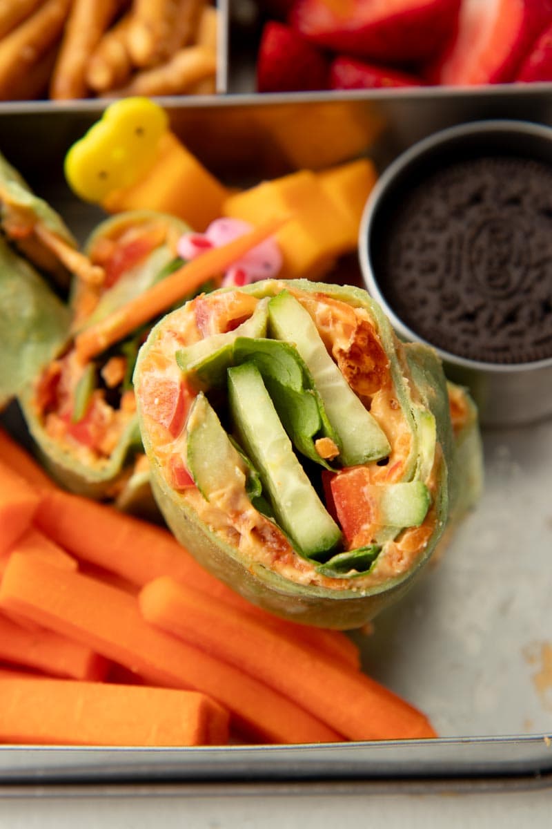 Close view of a veggie and hummus tortilla roll-up stacked in a three-compartment metal lunch container.