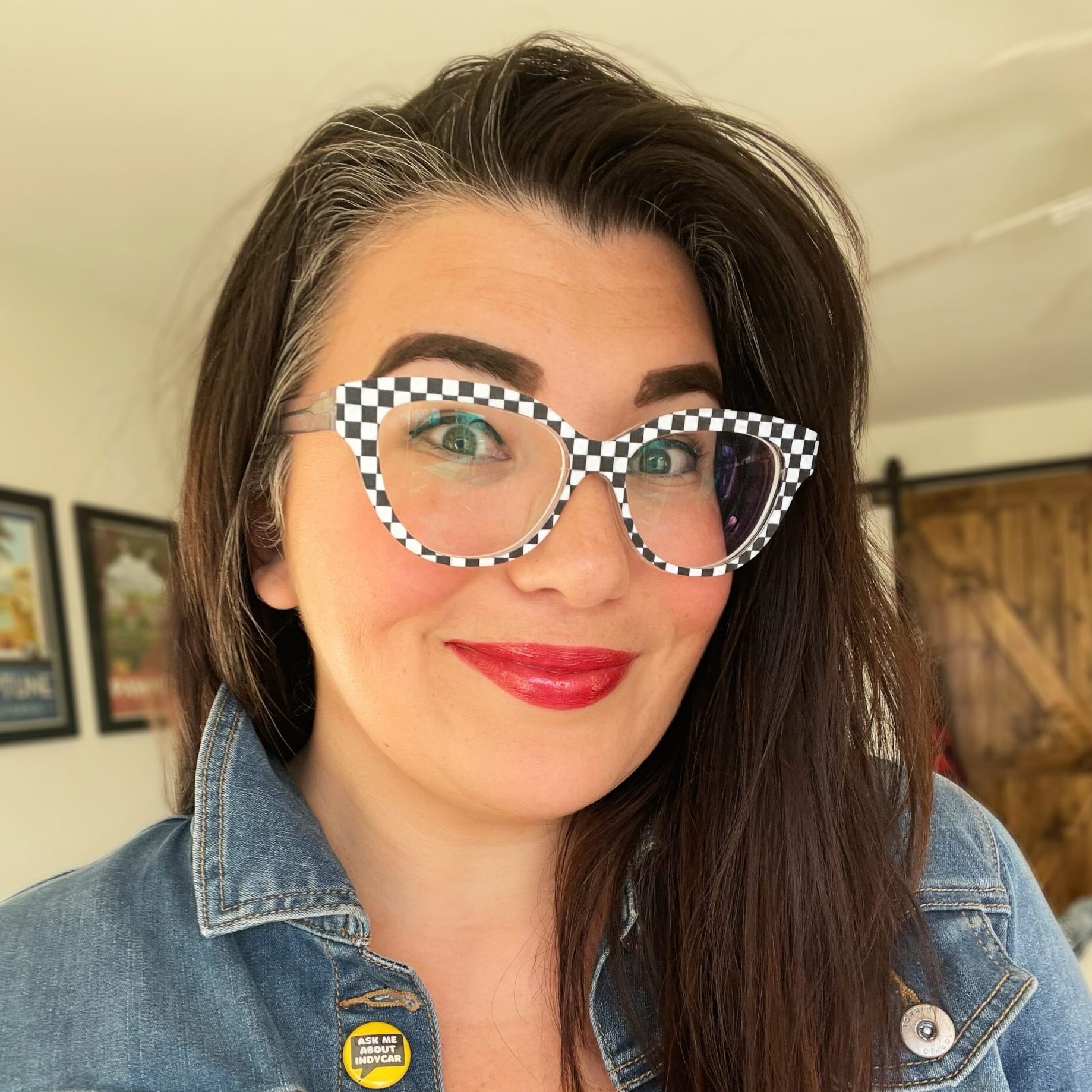 Cassie smiles to the camera while wearing checkerboard glasses and a denim jacket.