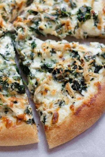 Chicken Spinach Alfredo Pizza, cut into slices on a white background.