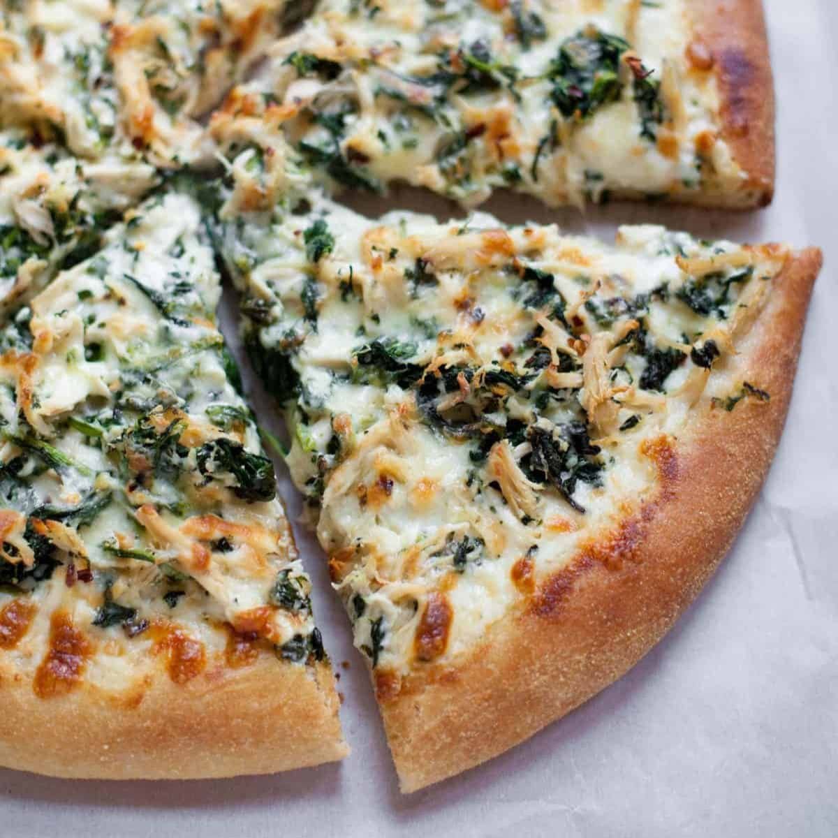 Chicken Spinach Alfredo Pizza, cut into slices on a white background.