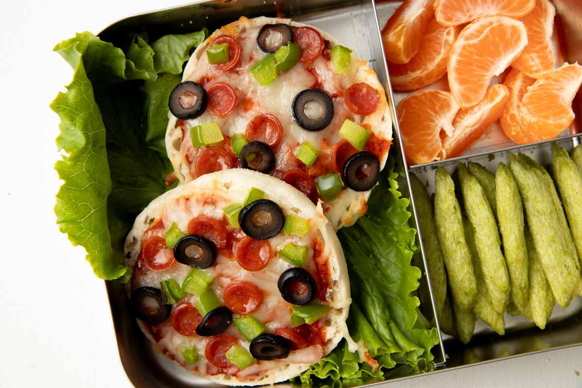Close view of two English muffin pizzas in a three-compartment metal lunch box.