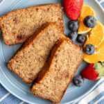 Banana bread slices on a blue plate with blueberries, a strawberry, and orange segments.