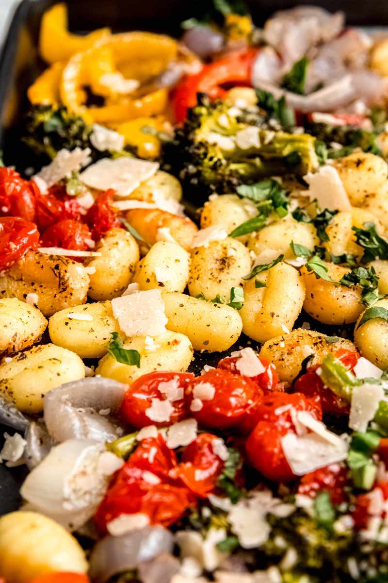 Close view of a tray bake with gnocchi and vegetables topped with shaved parmesan cheese.