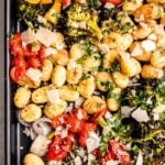 Top view of a dark sheet pan filled with baked gnocchi and vegetables topped with fresh basil and parmesan cheese.