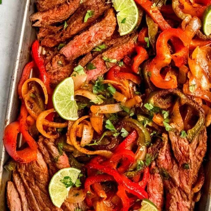 Top view of sheet pan steak fajitas garnished with lime wedges and chopped cilantro.