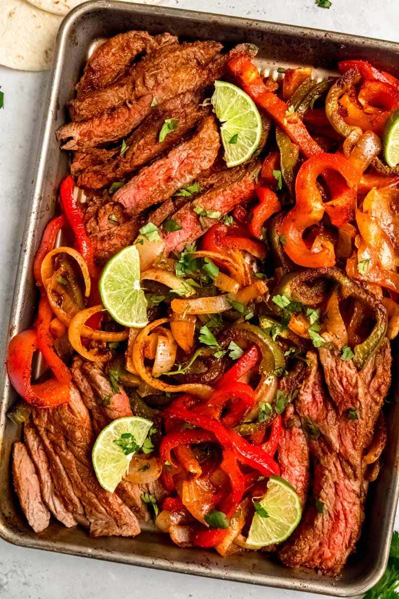 Top view of sheet pan steak fajitas garnished with lime wedges and chopped cilantro.