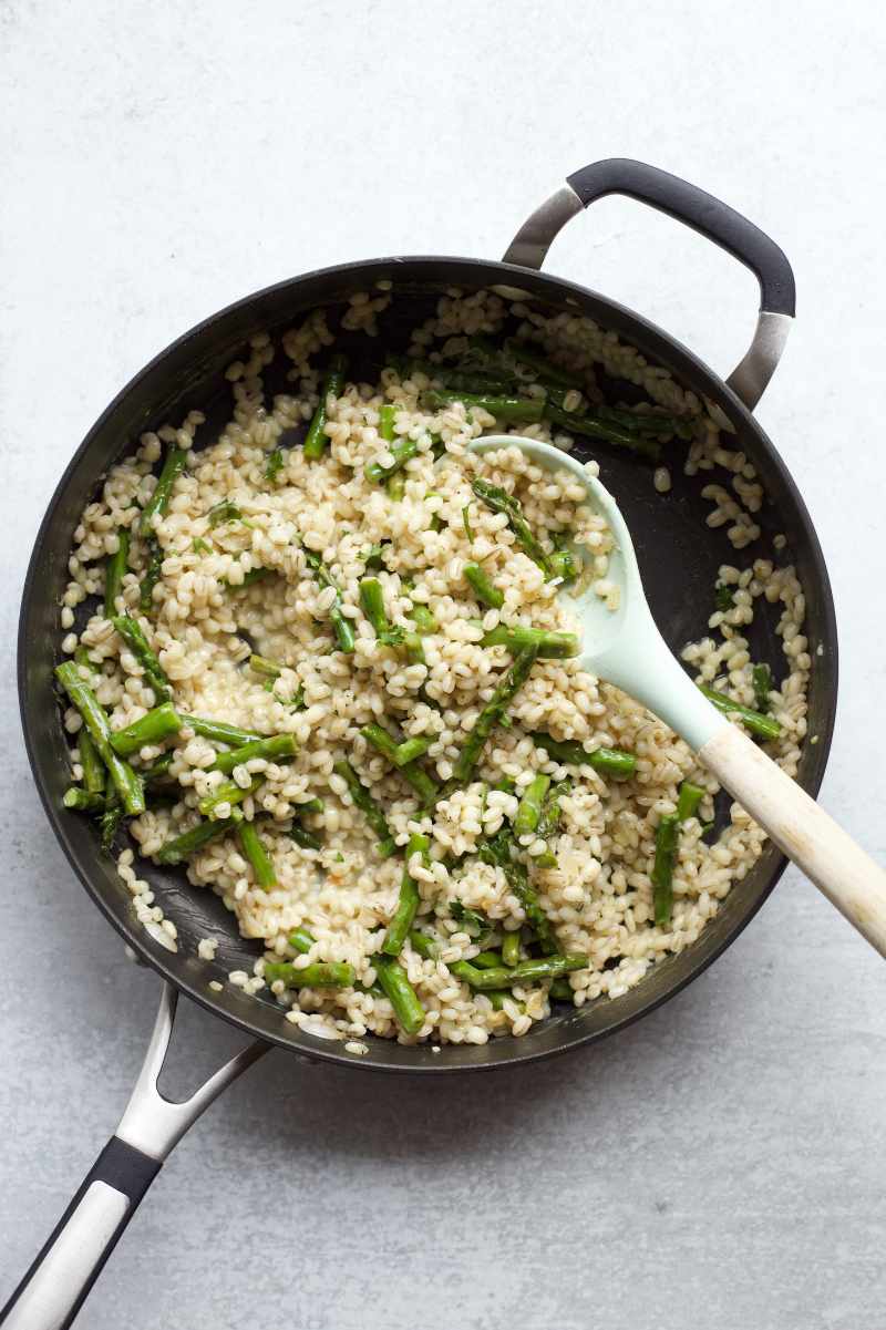Overhead of asparagus risotto in a skillet with a cooking spoon.