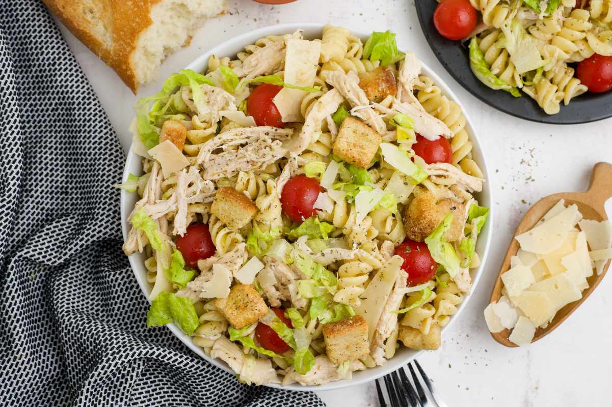 Top view of chicken caesar pasta salad dinner with bread, forks, and shaves parmesan around it.