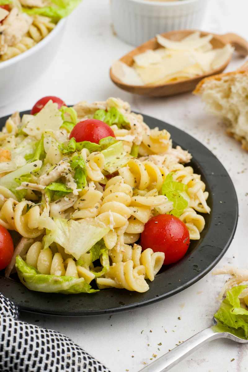 Chicken caesar rotini salad plated with bread and shaved parmesan alongside it.