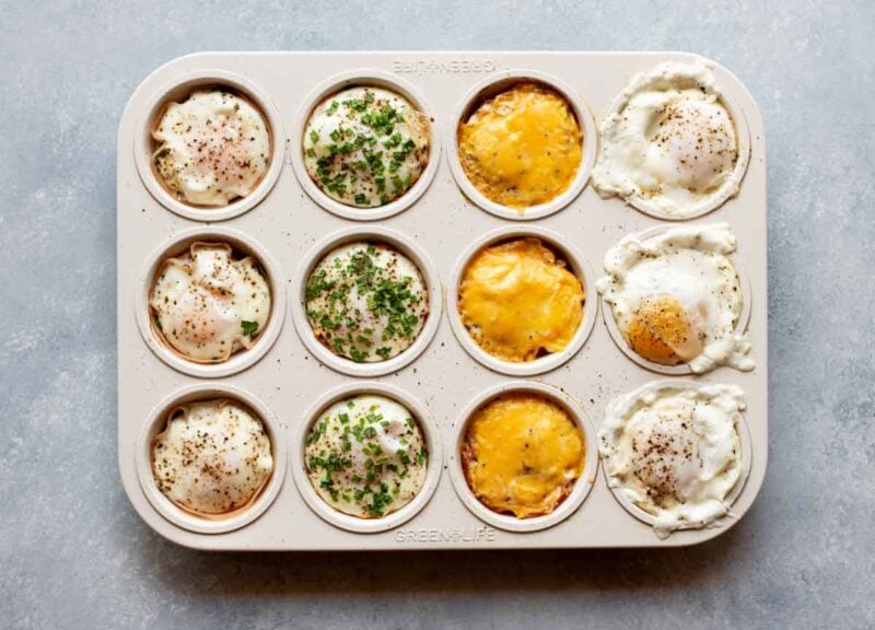 A muffin tin with cooked egg cups three of each variety, turkey spinach, sweet potato and chive, ham and cheddar, and caprese.