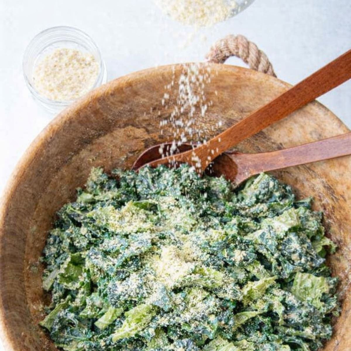 Grated parmesan being sprinkled over a bowl of kale caesar salad topped with roasted chickpeas.