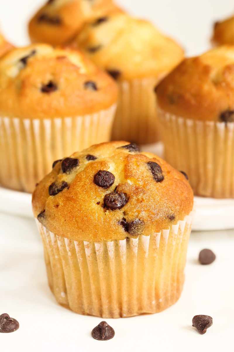 Close view of a mini chocolate chip muffin on a white counter with additional chocolate chips around it.