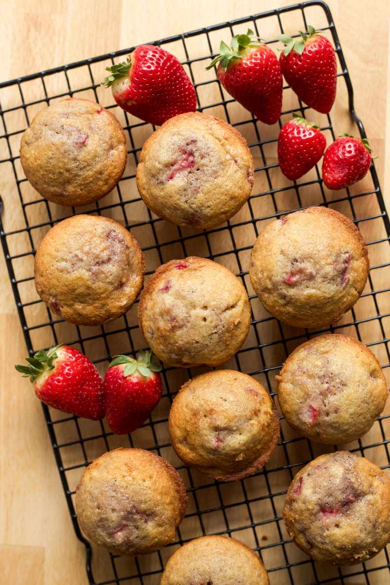 Overhead of muffins cooling on a wire rack with bright red berries around.