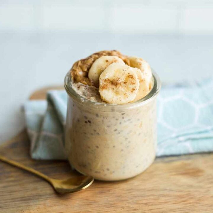 A small, gold, dessert spoon rests next to a jar of peanut butter banana overnight oats.