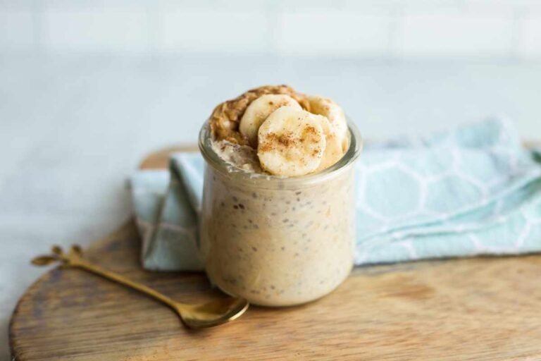 A small, gold, dessert spoon rests next to a jar of peanut butter banana overnight oats.