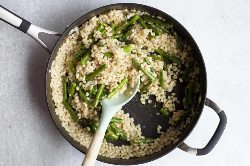A spoon scoops grains and veggies from a skillet.