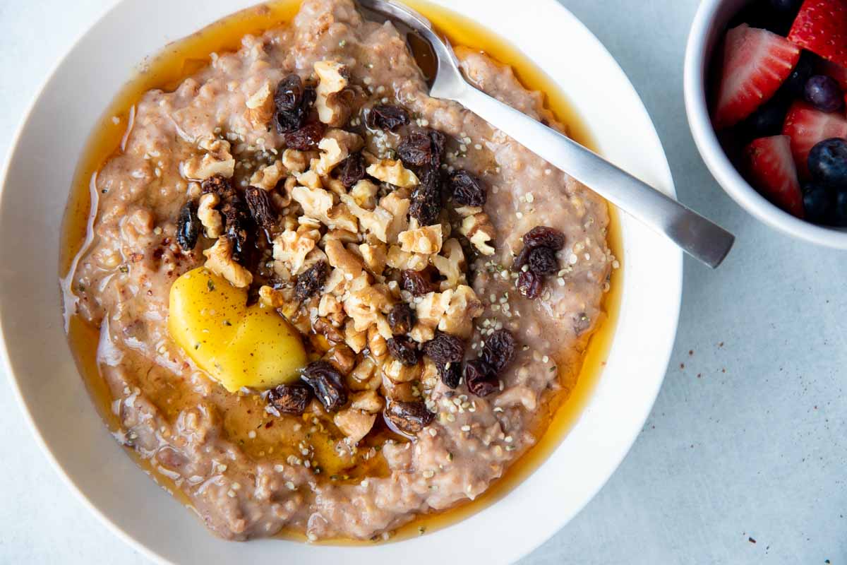 A bowl of slow cooker steel cut oats garnished with butter, maple syrup, dried fruit, and nuts.