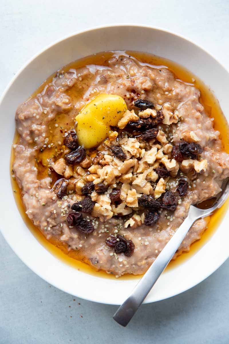 Overhead of a single serving of slow cooker steel cut oats in a bowl drizzled with maple syrup and topped with chopped walnuts and dried fruit.