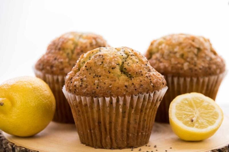 A trio of poppyseed muffins on a white background with bright citrus fruit nearby.