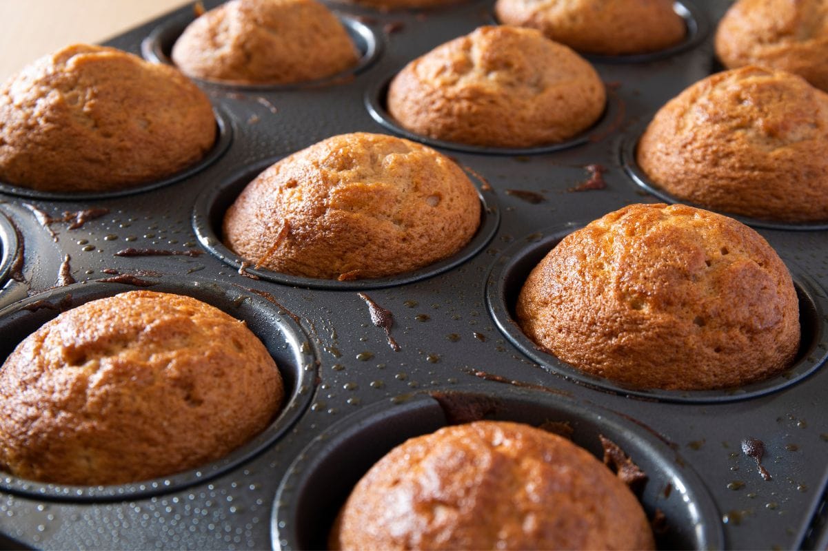 Tight view of apple cinnamon muffins in a muffin tin showing the bakery-style domed tops.