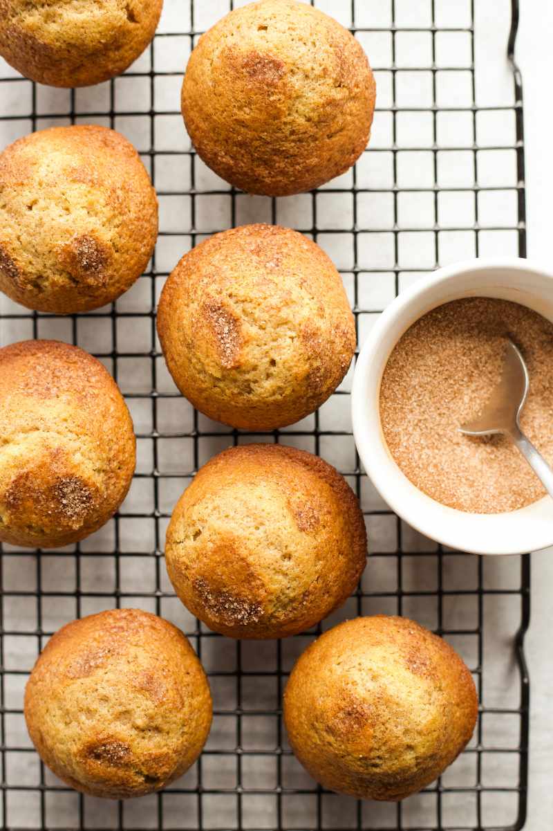 Cinnamon sugar muffins on a cooling rack with a small bowl of cinnamon sugar beside them.
