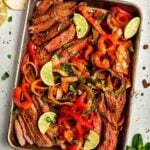Slices of cooked steak and bell peppers cooked on a sheet pan with lime wedges