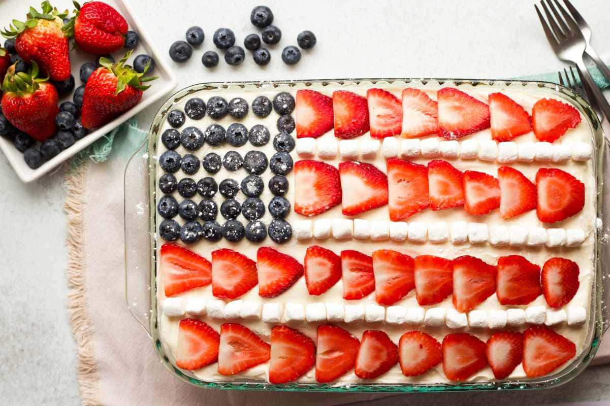 Berries rest alongside a glass baking dish with a cake decorated to look like the American flag.