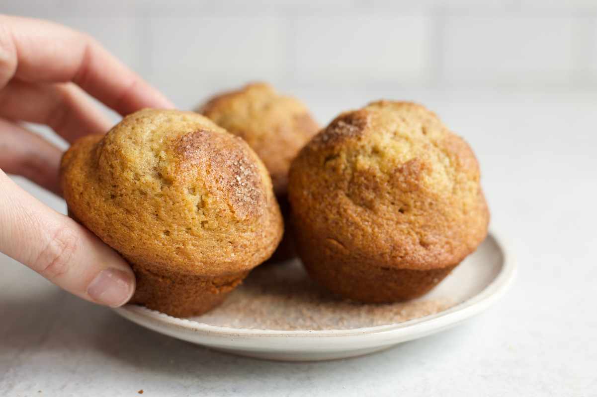 Close view of a hand taking a cinnamon muffin from a small serving plate.