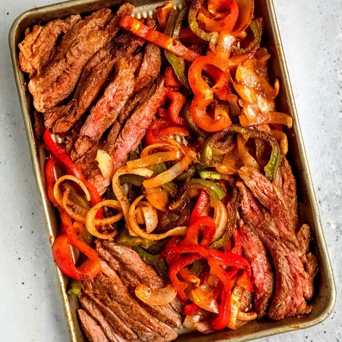 Sliced steak fajitas and peppers on a sheet pan