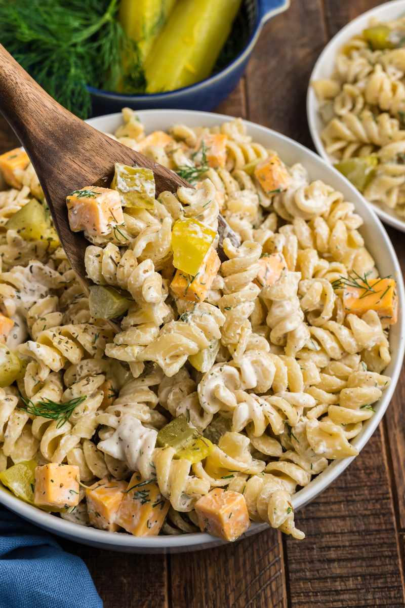 A wooden spoon digs into a bowl of creamy pasta salad.