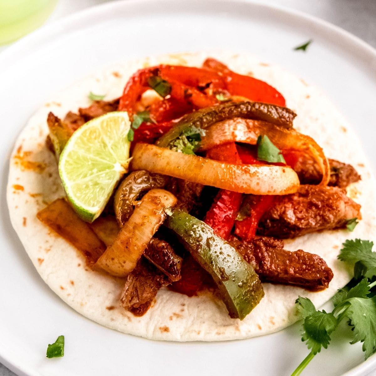Plate of sheet pan steak fajitas in a tortilla with lime wedge