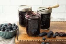 Three half-pint jars of berry jam stand on a wooden cutting board with fresh berries around them.