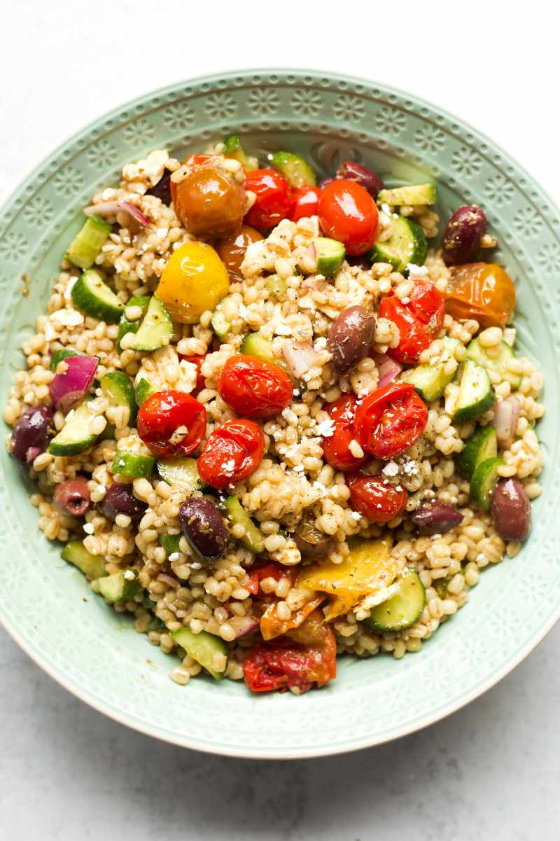 Top view of a decorative bowl filled with greek barley salad garnished with crumbled feta and dried oregano.