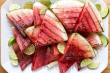 Lime slices are tucked around grilled watermelon slices on a white serving dish.
