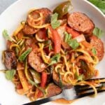 Close view of sausage and peppers served with zoodles on a round white plate.